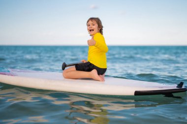 Çocuk ayakta raket üzerinde yüzüyor. Su sporları, aktif yaşam tarzı. Okyanusta kürek çeken bir çocuk var. Çocuk Paddle binicisi. Yaz Suyu sporu, SUP sörfü. Yaz tatili