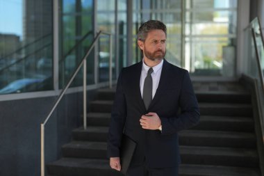 Businessman standing outdoor on modern office building. Business success. Business man thinking outdoor. Modern businessman in full suit standing outdoors near office cityscape