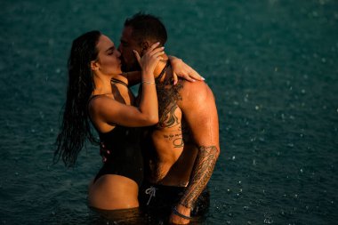 Sudaki seksi çiftin romantik yaz fotoğrafı. Deniz suyunda romantik çift kucaklaşması. Yaz öpücüğü. Çift yağmurda öpüştü. Şehvetli çift yağmurun altında öpüşüyor.