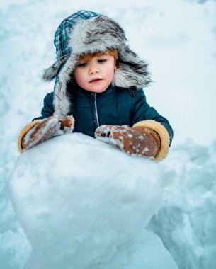 Heyecanlı çocuk kış portresi. Çocukların duyguları. Çocuklar için kış kıyafetleri. Neşeli çocuk kış parkında kardan adamla eğleniyor.