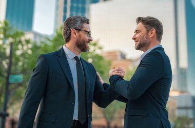 Şehir caddesinde el sıkışan iki işadamı. Takım elbiseli işadamları dışarıda el sıkışıyor. İki işadamı arasında tokalaşma. Selamlama, anlaşma, birleşme ve satın alma kavramı