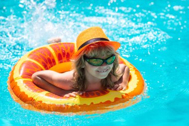 Yüzme havuzunda şişme yüzük takan çocuk. Çocuklar turuncu yüzgeçle yüzerler. Su oyuncağı, çocuklar için sağlıklı açık hava sporları. Çocuklar plaj eğlencesi. Yaz su havuzunda su sıçratan çocuk