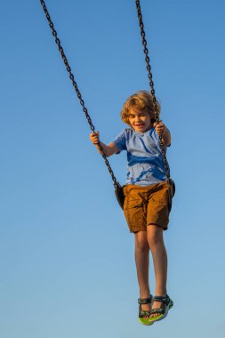 Zincirle sallanan küçük çocuk şehir çocuklarının oyun alanında sallanıyor. Sallanma turu. Salıncakta salıncakta sallanan tatlı bir çocuk. Sarışın küçük çocuk çocuk parkında sallanıyor. Yüksekten sallanan çocuk