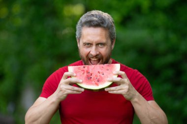 Karpuzlu komik erkek suratı, yaklaş. Yazlık parkta karpuz yiyen heyecanlı bir adam. Karpuz yiyen bir adam. 40 'ların adamı dışarıda meyve yiyor. Karpuz seven bir adam
