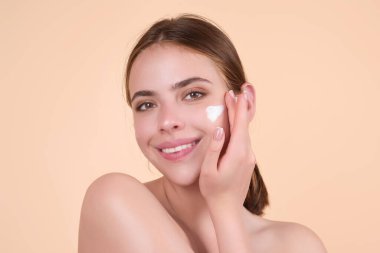 Young woman applying body cream against studio background. Beauty routine. Studio face of a beautiful woman with perfect skin. Wrinkle cream. Concept of beauty. Woman applying face cream