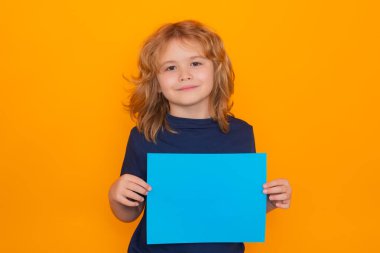 Sarı arka planda izole edilmiş, boş mavi kağıtlı sevimli bir çocuk. Elinde boş bir levha olan bir çocuğun portresi, poster. Model, kopyalama alanı