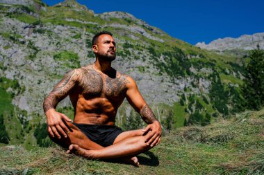 Seksi fit adam meditasyonu. Spor mankeni doğada rahatlar. Meditasyon, ruhsal sağlık. Sakin bir meditasyon adamı farkındalığı eğitiyor. Rahatlayın ve doğada meditasyon yapın. Sakin ol ve doğada rahatla.