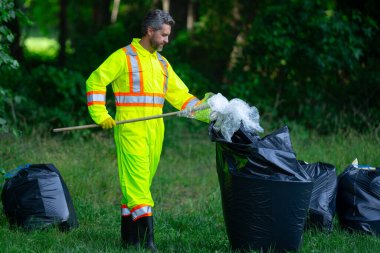 Üniformalı adam temizlik için çöp plastiği topluyor. Çöpleri toplayan adam. Çöp şişeleri toplandı. Plastik atık. Çöp toplama, çevre. Ekoloji, kirlilik, plastiklerden temizlik