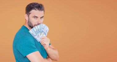 Bej rengi stüdyo ve pankartta para saklayan yakışıklı bir adam. Dolar banknotları halinde para. Yığınla para, finans, yatırım ve tasarruf. Model pankartı