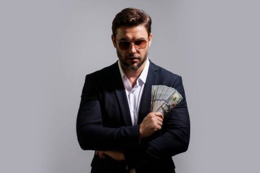 İyi ödeme. Yakışıklı adam gri stüdyoda izole edilmiş para tutuyor. Dolar banknotları halinde para. Yığınla para, finans, yatırım ve tasarruf. Model pankartı
