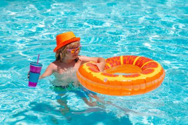 Havuzda yüzen çocuk yüzen yüzükle oynuyor. Yaz çocukları kokteyli. Güneş gözlüklü sevimli çocuk yaz günü havuzda şişirilebilir yüzüklerle yüzer.