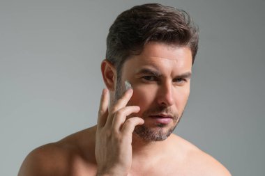 Amerikalı bir adam kırışıklığa yüz kremi sürüyor. Sabah güzellik rutini. Kırışık derili bir adam. Yaşlanma önleyici ve kırışıklık önleyici krem. Erkek güzelliği kavramı. Kırışık cilde krem süren adamın yüzünü kapat.