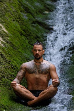 İnsan meditasyonu. Spor mankeni doğada rahatlar. Meditasyon, ruhsal sağlık. Sakin bir meditasyon adamı farkındalığı eğitiyor. Rahatlayın ve doğada meditasyon yapın. Sakin ol ve doğada rahatla.