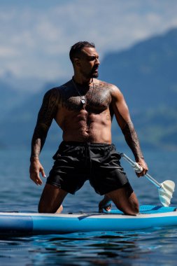 Erkek, kürek tahtası ile güçlü kas modeline uyuyor. Kürek çeken bir adam. Sağlıklı yaz yaşam tarzı. Su sporu. İsviçre 'deki Alps Gölü' nde yaz tatilinde SUP sörfü
