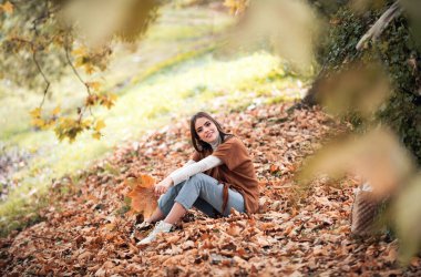 Sarı akçaağaç yapraklı neşeli bir kadının sonbahar portresi. Yaprakları sonbahar yapraklı güzel kız portresi. Sonbahar yapraklarının yanında güzel bir kızın portresi. Romantik şefkat kadını