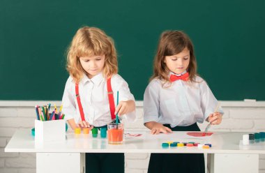 Çocukların yaratıcı gelişimi. Okulda resim çizen ve resim yapan sevimli okul arkadaşları. Dost canlısı bir oğlan ve komik öğrenciler çizer. Okulda arkadaşlık.