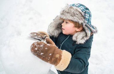 Mutlu çocuk beyaz kış arka planında kartopuyla oynuyor. Küçük çocuk kış parkında kardan adamla oynuyor. Kardan adam ve kardaki komik küçük çocuk
