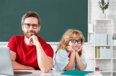 Eğitim ve öğrenme kavramı. İlkokul öğrencisinin dersi var. Öğretmeni olan çocuk İngilizce ya da matematik öğreniyor. Baba ve oğul okulda ödev yapıyor.