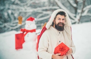 Noel tebrik kartı. Noel Baba mutlu Noeller diliyor. Kış tatilin kutlu olsun. Uzun sakallı, Noel kar arka planında poz veren stil sahibi Noel Baba hipster.