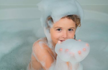 Çocuklar banyo yapıyor. Çocuk köpüklerle banyoda eğleniyor. Mutlu çocuk banyonun tadını çıkarıyor. Küçük çocuk sabun köpüğüyle banyoda gülümsüyor. Çocuk köpükle banyo yapar.