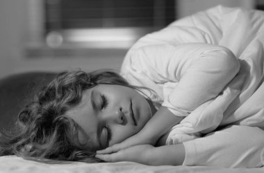 Yatakçı çocuk. Çocuk kestiriyor. Yatakta uyuyan çocuk, yatak odasında rahat bir yatak. Sağlıklı uyku konsepti. Yumuşak yastık, rahat, rahat yatak