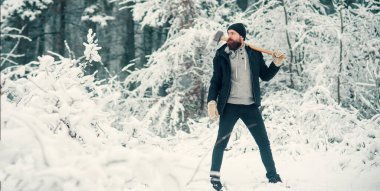 Oduncu baltayı tutuyor. Sakallı hippi, ciddi yüzlü ve baltalı. Kışın açık havada vahşi bir oduncu. Karlı ormanda oduncu hippi. Kışlık pankart için oduncu