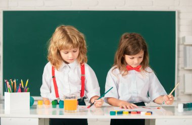 Funny pupils draws in classroom on school blackboard background. School friends kids painting together in class