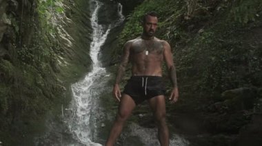 Su doğasında rahatla. Dağ şelalesinin altındaki adam, su sıçratmayı seviyor. Doğada yıkanmak. Tropikal doğada şelaledeki güçlü zinde adam. Açık havada kaslı bir İspanyol.