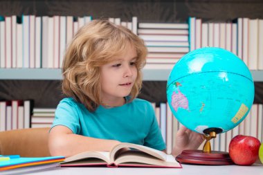 School kid pupil looking at globe in library at the elementary school. World globe. School kid 7-8 years old with book go back to school. Little student. Education concept