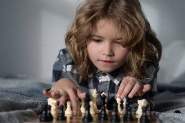 Çocuk yatakta satranç oynuyor. Akıllı konsantre ve düşünen bir çocuk satranç oynuyor. Çocuk satranç stratejisi geliştiriyor, masa oyunu oynuyor