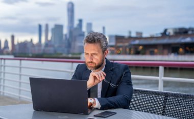 New York 'ta ofis binasının yakınında dizüstü bilgisayarda çalışan serbest çalışan bir adam. İş ve serbest çalışma. İş portresi. Dışarıda dizüstü bilgisayarla çalışan bir iş adamı. Olgun yaş, orta yaş, 50 'li yaşlar