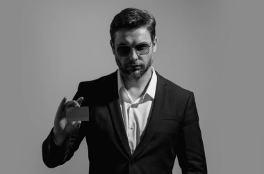 Elinde kredi kartı tutan yakışıklı bir adam. Gri stüdyo geçmişinde kredi kartı olan orta yaşlı bir adam. Kredi kartı konsepti. Takım elbiseli bir işadamı kredi kartıyla ödeme yapıyor.