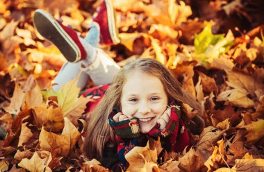 Altın akçaağaç yapraklı çocuk. Yapraklarla oynamak. Güzel, mutlu bir kız çocuğu sonbahar parkında yaprakların arasında eğleniyor. Pozisyon
