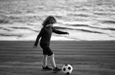 Futbol topuyla spor giyim sektöründe genç bir futbolcu. Neşeli küçük çocuk futbolun, gün batımında futbol maçlarının tadını çıkarıyor.