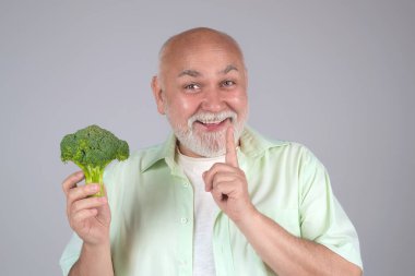 Sebze Diyetinde son sınıf. Sebzeler. Yaşlı, olgun bir adam sağlıklı yiyecekler yiyor, diyet yapıyor. Son sınıf öğrencisi stüdyoda brokoli tutuyor. Vejetaryen salatası. Diyette olgunlaşmak. Yıllanmış diyet. Sağlıklı yiyecekler. Kilo kaybı için diyet