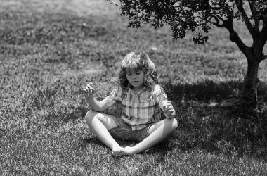 Çocuk güneşli yaz gününde gözleri kapalı parktaki yeşil çimenler üzerinde meditasyon yapıyor. Meditasyon, hayal, refah ve sağlıklı çocuk yaşam tarzı kavramı. Özgürlük ve kaygısız çocuklar