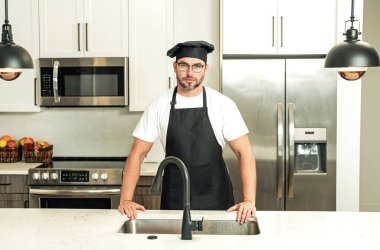 Mutfakta şef üniforması giyen yakışıklı orta yaşlı bir adam. Aşçılık ve aşçılık. Restoran menüsü konsepti. Yemek servisi, yemek pişirme, yemek reklamcılığı. Üniformalı adam mutfakta.
