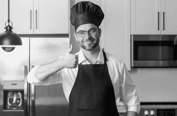 stock image Happy baker with thumb up. Portrait of chef man in a chef cap in the kitchen. Man wearing apron and chefs uniform and chefs hat. Character kitchener, chef for advertising