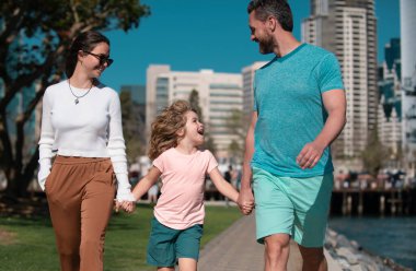 Genç çift oğluyla birlikte şehir parkında yürüyor. Küçük oğlu olan mutlu bir aile şehirde yürüyor.