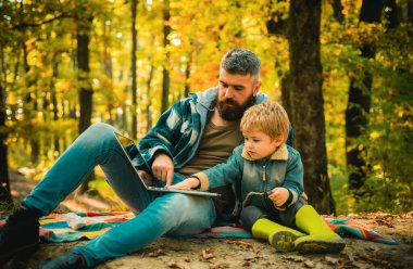 Father and his toddler son walking during the hiking activities in autumn forest. Active family time on nature. Fun with little kids in fall days. Dad and son walking at autumnal park concept clipart