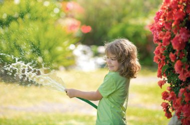 Küçük mutlu çocuk ev bahçesinde eğleniyor. Çocuk bahçe hortumunu tutuyor. Hasat zamanı arka bahçede çocuklar için açık hava oyunları..