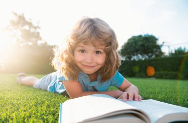 Zeki çocuk yeşil çimenler üzerine kitap okuyor.
