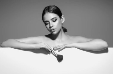 Beautiful young woman apply powder on face. Beauty Makeup. Portrait of female model with cosmetic brush. Perfect soft skin and natural makeup. Applying powder blush highlighter, foundation tone