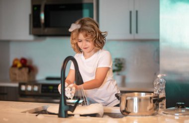 Mutfakta bulaşık yıkamaya yardım eden komik ikiz çocuklar. Çocuklar ev işleriyle eğleniyor. Mutfakta lavabonun yanında bulaşık yıkayan tatlı bir çocuk.