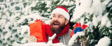 Noel Baba kışın karlı arka planda hediye kutusuyla heyecanlanıyor. Noel Baba şapkalı, açık havada Noel hediyeli bir adam. Karlı kış arkaplanı. Noel Baba dışarıda kar yağışı altında hediyeler taşıyor.