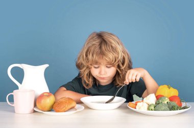 Çocuk çorba içiyor. Küçük bir çocuğun portresi çorba yerken ya da kahvaltı yaparken masada kaşıkla yemek yerken.