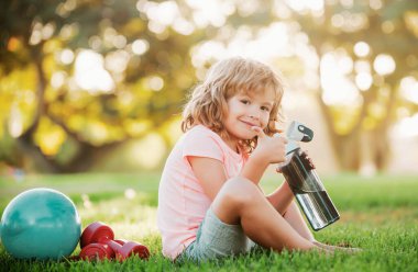 Fitness çocuğu. Parkta spor şişe suyu olan küçük bir çocuğun portresi. Jimnastik. Çocuk sporcusu, çocukluk aktivitesi. Çocuklar spor ve spor