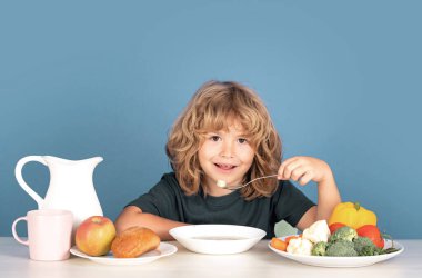 Tatlı, mutlu çocuk öğle yemeğinde çorba içiyor. Çorba içen çocuk. Stüdyonun arka planında sağlıklı yiyecekler yiyen çocuk