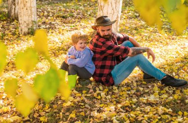Mutlu erkek bebek ve şapkalı sakallı baba düşen sarı sonbahar yapraklarının üzerinde oturuyor. Baba ve oğul parkta iyi vakit geçiriyorlar. Doğada aktif aile zamanı. Sonbahar günlerinde küçük çocuklarla eğlenmek