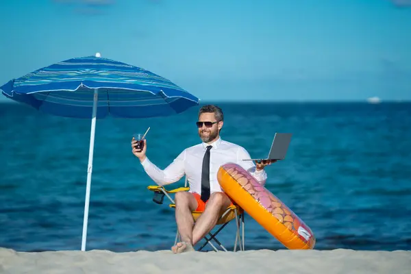 stock image Successful businessman on summer vacations. Funny business man drink summer cocktail and using laptop in sea beach. Summer business concept. Hot summer. Crazy work. Remote online working